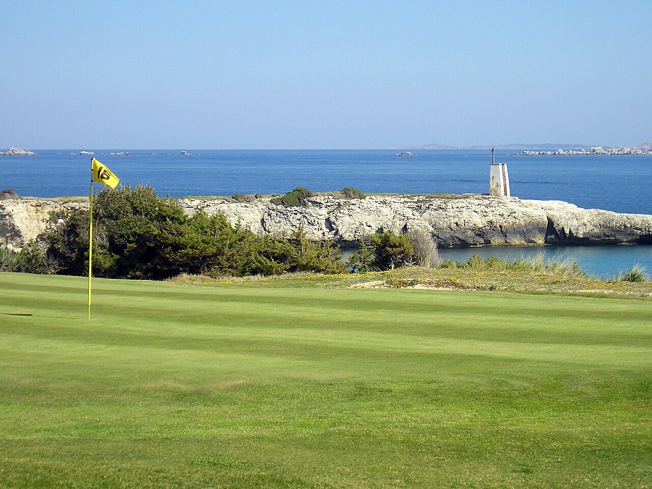 A coastal golf green with a yellow flag, blue sea behind