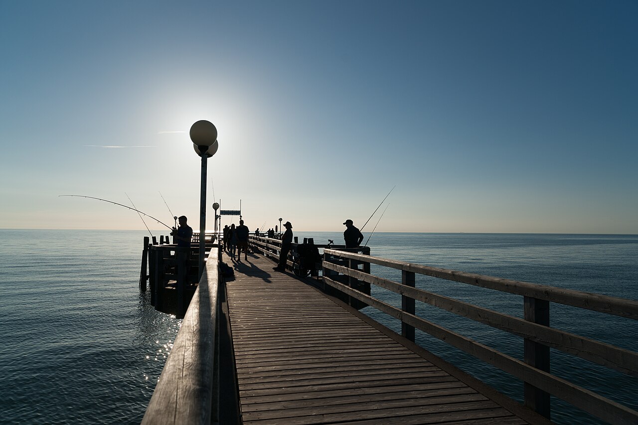 Anglers in silhouette on a long pier reaching into the Channel at sunrise