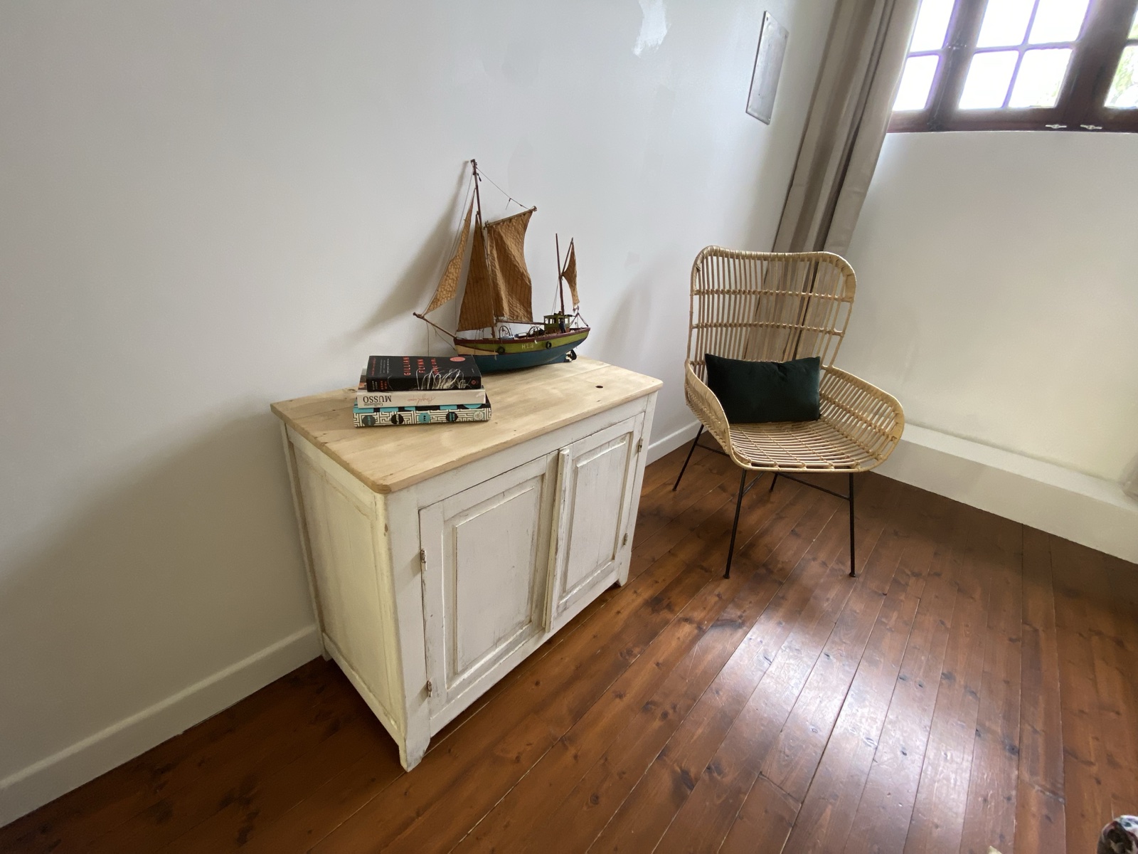 A model sailboat, vintage books and rattan reading chair beside a window