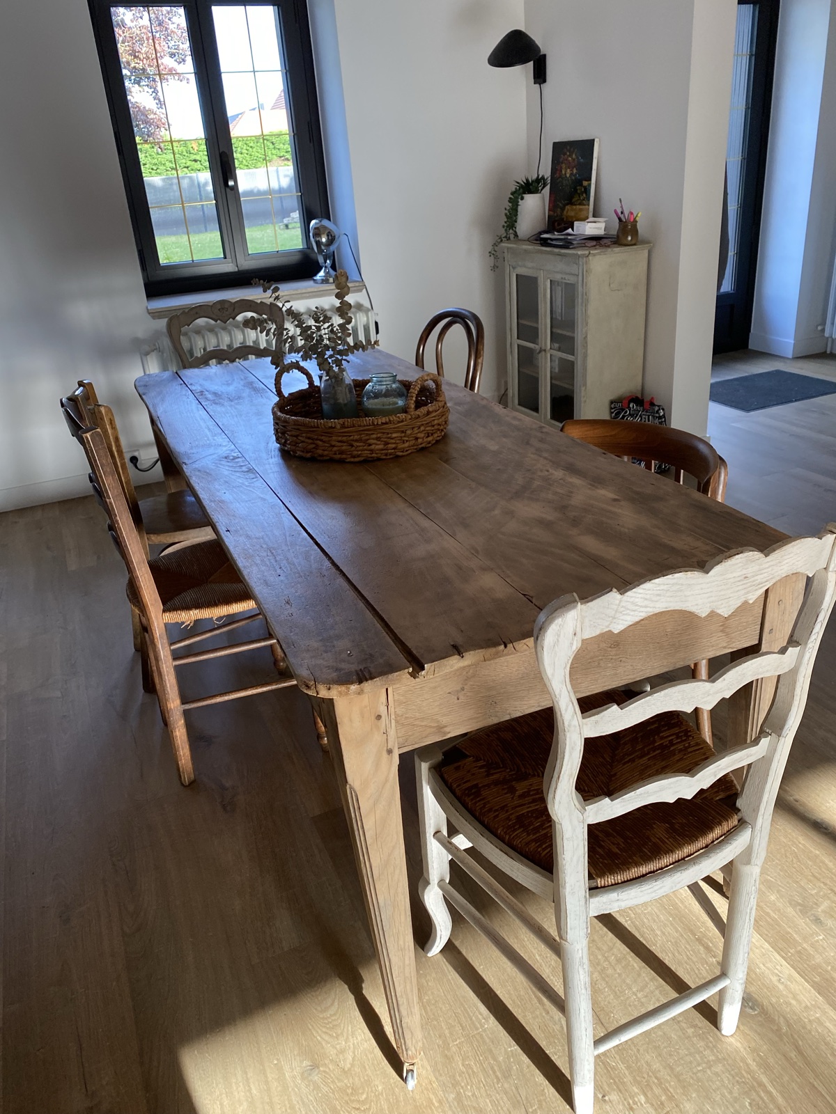 The long farmhouse dining table with mixed antique chairs, woven tray and view to the garden window