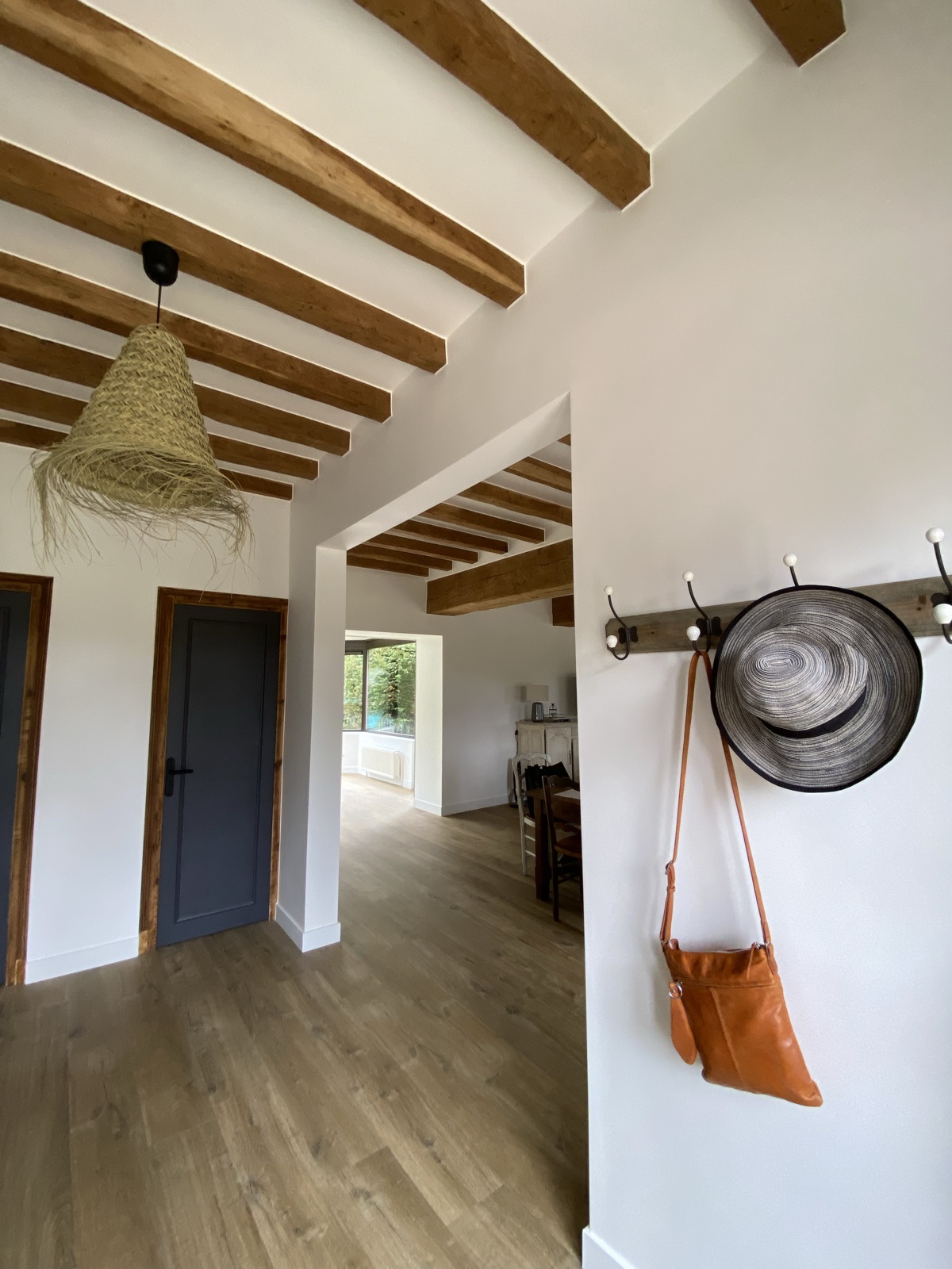 Beamed entry hall with a sun hat and tan leather satchel on coat hooks, view through to the dining area