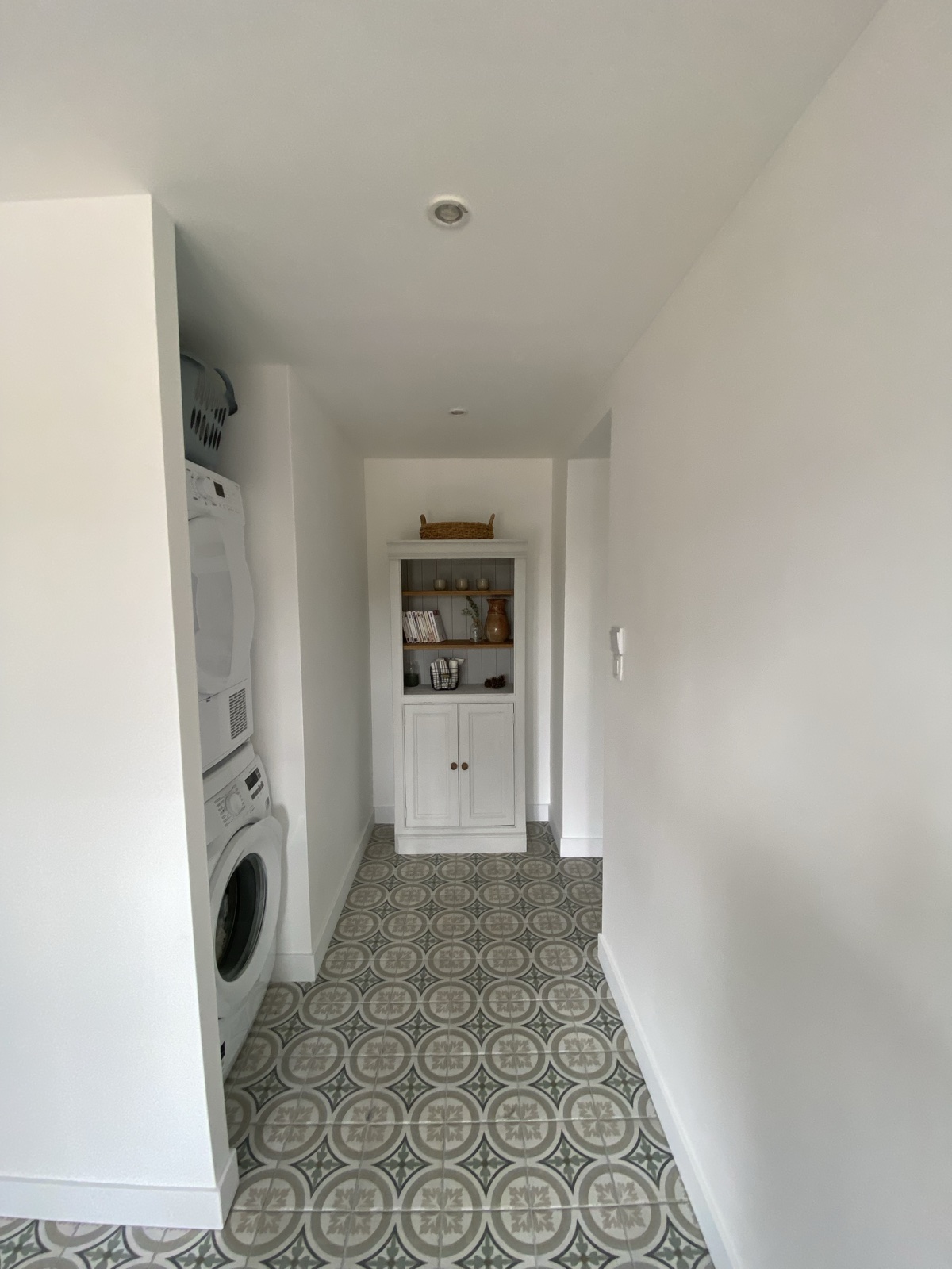 Laundry corridor with stacked washer and dryer, built-in cupboard and patterned cement-tile floor